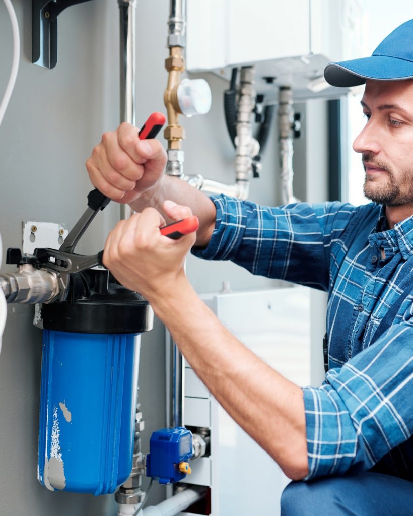 young plumber or technician installing or repairing system of water filtration